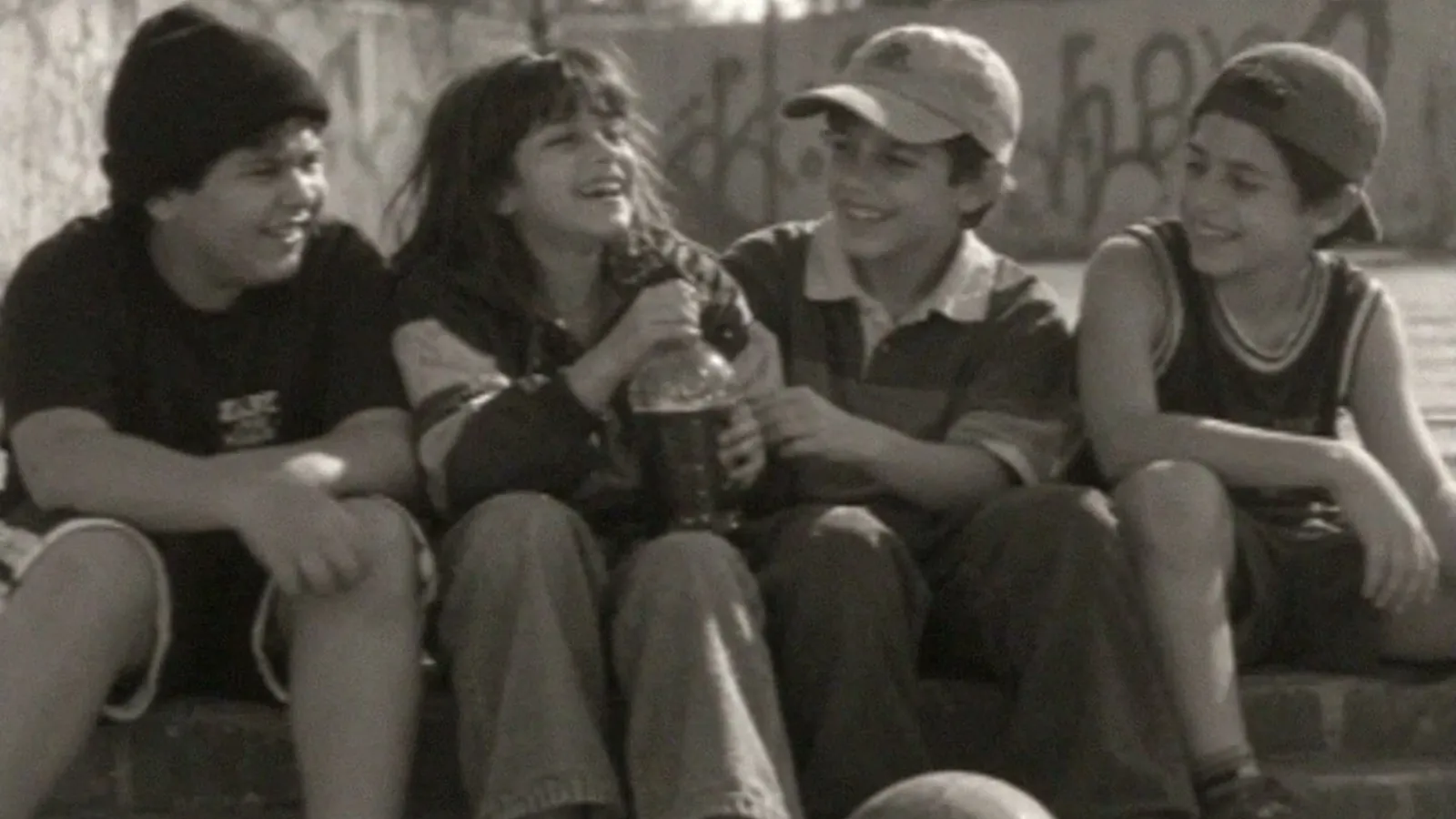 Four kids sitting on a step, laughing, in black and white with a VHS texture